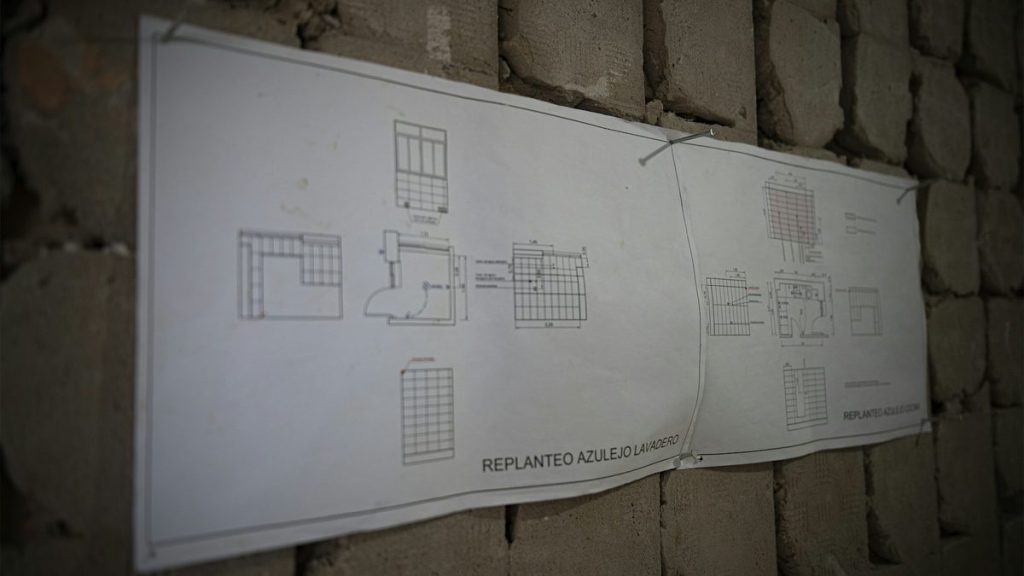 Planos de replanteo de una reforma integral de piso colgados en la pared de obra en Zaragoza